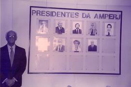 Fotografia de Everardo Moreira Lima ao lado do quadro dos ex-presidentes da AMPERJ